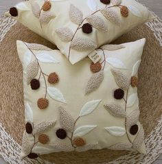 two decorative pillows sitting on top of a woven basket next to a pillow with leaves