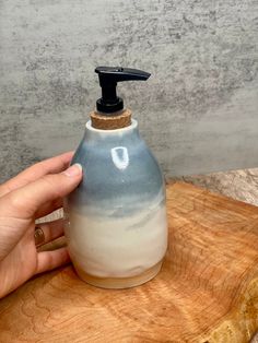 a hand holding a soap dispenser on top of a wooden board