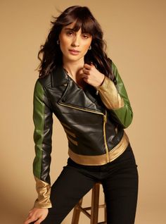 a woman sitting on top of a stool wearing a black and green jacket with gold accents