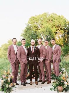 a group of men standing next to each other in front of flowers and greenery