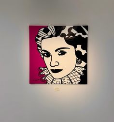 a woman's face is shown on a pink and black painting hanging on the wall