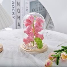 a pink crocheted flower in a glass dome on top of a white table