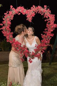 two women standing next to each other in front of a heart shaped frame with flowers