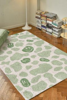 a green and white rug on the floor in front of a lamp with bookshelves behind it