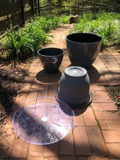 two planters sitting next to each other on a brick walkway in front of some plants