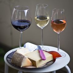 three glasses of wine and cheese are sitting on a small table with a white plate