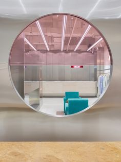 a round mirror reflecting the inside of a room with blue chairs and a table in front of it