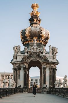 a woman is standing in front of an ornate archway with gold decorations on top and the sky above her