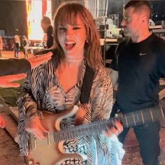 a woman playing an electric guitar while standing next to a man in a black and white shirt