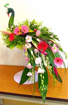 a vase filled with flowers on top of a wooden table next to a green bird