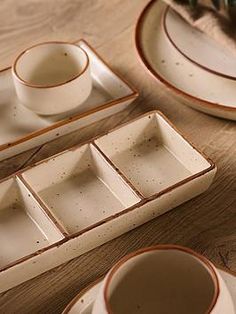 an assortment of white dishes and cups on a wooden table with flowers in the background