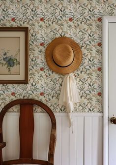 a hat is hanging on the wall next to a wooden chair and framed painting in a room