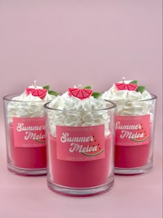 three glass cups filled with whipped cream and topped with green leaves on pink background next to each other