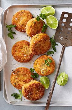 some fried food on a tray with limes and a spatula next to it