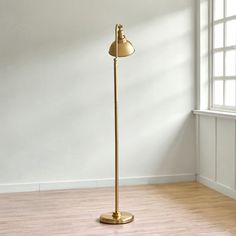 a floor lamp in an empty room with white walls and wooden floors, near a window