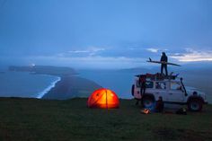 a man standing on top of a vehicle next to a tent with a surfboard