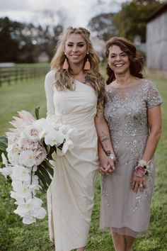 two women standing next to each other in front of a field with flowers and grass