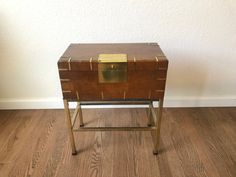 an old trunk is sitting on a metal stand in front of a white wall and wood floor