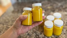 a woman holding five jars of yellow liquid