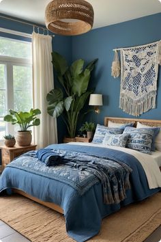 a bed with blue sheets and pillows in a bedroom next to a large potted plant