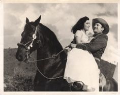 a man and woman riding on the back of a black horse in an old photo