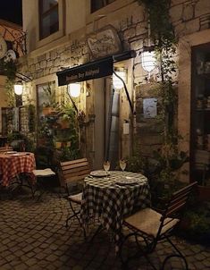 an outdoor dining area at night with tables and chairs covered in checkered tablecloths