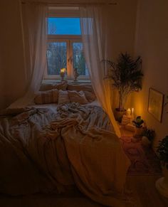 an unmade bed sitting in front of a window next to a potted plant