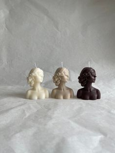 three small candles are sitting in the shape of women's heads on a white background