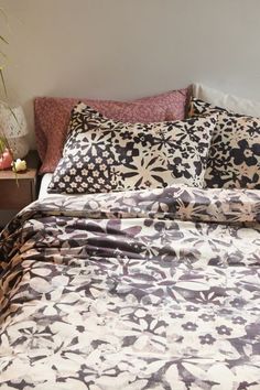 a bed with black and white patterned comforter next to a night stand filled with flowers