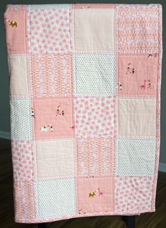 a pink and white patchwork baby quilt on a black wooden chair in front of a wall