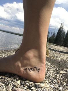 a person's foot with a small mountain tattoo on the side of their leg