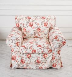 a chair with floral fabric on it in front of a white wall and wooden floor