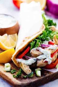 a pita sandwich with chicken, lettuce, and tomatoes on a cutting board