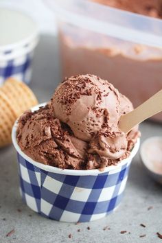 a scoop of chocolate ice cream in a blue and white checkered cup with a wooden spoon