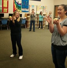 two girls are playing with an apple while others watch from the back ground in a classroom