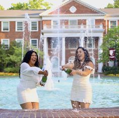 two women in white dresses are playing with each other near a fountain and brick building