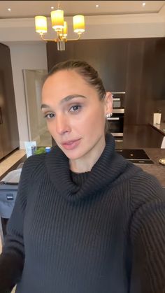 a woman is taking a selfie in the kitchen while wearing a turtle neck sweater