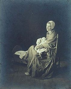 an old black and white photo of a woman sitting in a chair holding a baby