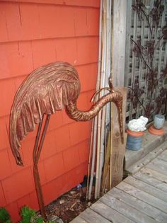 a metal flamingo standing next to a red building