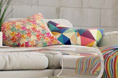 a white couch with colorful pillows sitting on it's back cushions and a potted plant in the corner