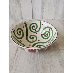 a white bowl with green and red designs on the rim sitting on a wooden surface