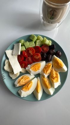 a plate with eggs, tomatoes, cucumbers and olives next to a cup of coffee