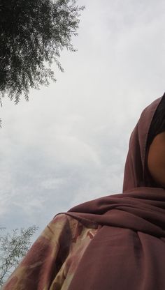 a woman wearing a red and gold shawl looking up into the sky with trees in the background