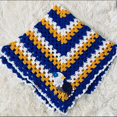 a blue and yellow crocheted blanket laying on top of a fluffy white rug