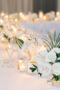 the table is set with white flowers, candles and greenery in glass vases