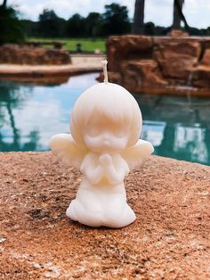 a little angel figurine sitting on top of a rock next to a pool