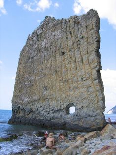 two people are sitting on rocks near the ocean and one is looking at an open hole in the rock