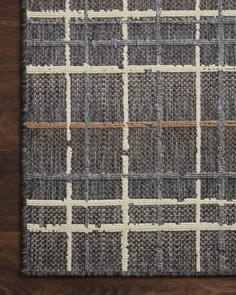 an area rug with grey and white plaid pattern on top of wooden flooring next to a wall