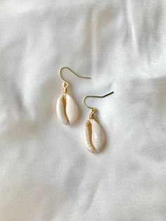 two seashells are hanging from gold earwires on a white cloth background