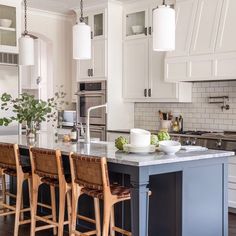 a kitchen with white cabinets and an island in front of the countertop, surrounded by stools